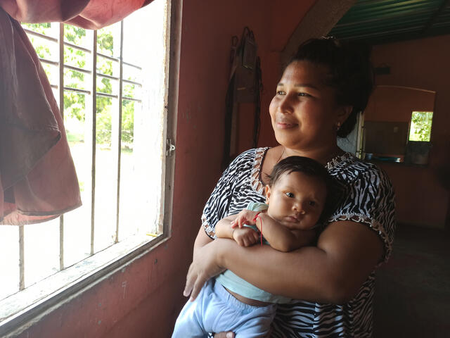 New mother Michel, holding baby Nathan, smiles as she looks out the window of her home in Venezuela.