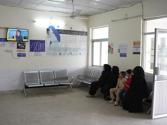 Patients sitting inside a waiting room, watching animated messaging around hygiene protocols on TV