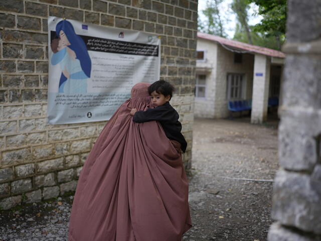 A woman wearing a veil carries her son in her arms as she heads towards the IRC's EU-funded health facility
