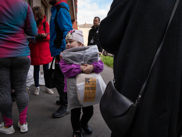 A young girls stands in a crowd, holding a blanket distributed by the IRC.