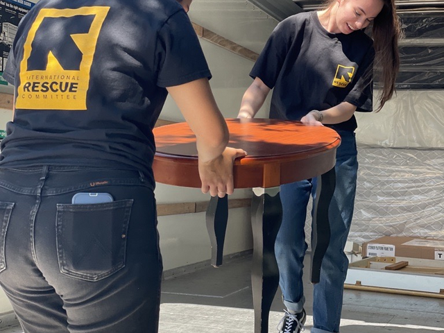 Two IRC staff members carry a coffee tables out of a u-haul