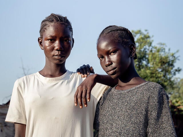 Sisters Muna and Khamis live with their mother in an IDP camp in South Sudan. Here, they pose for a photo outdoors.