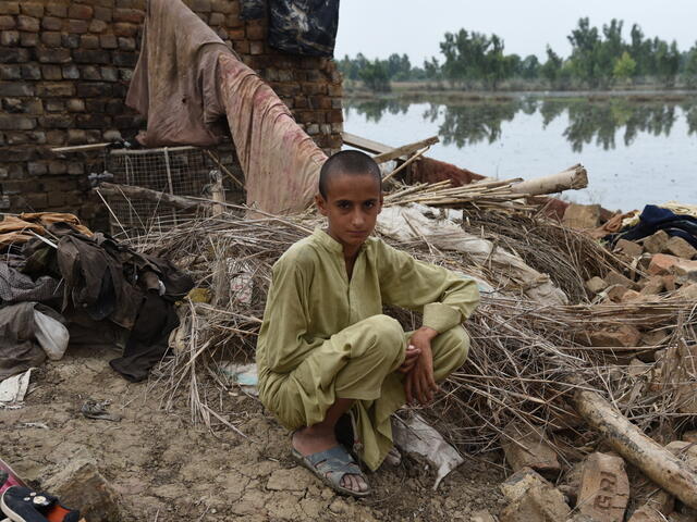 A young Pakistani boy sitting in front of his home ruined by floods