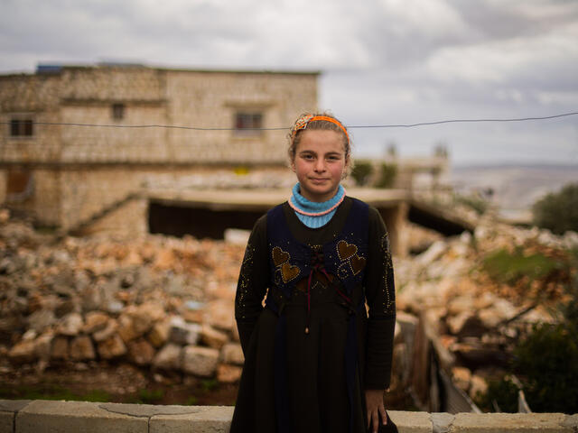 Little girl standing in front of the ruins of her family home