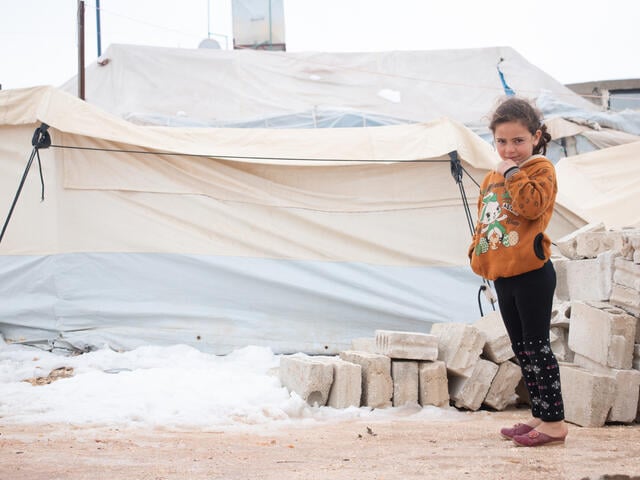 A little girl stands in front of her family's tent in Syria