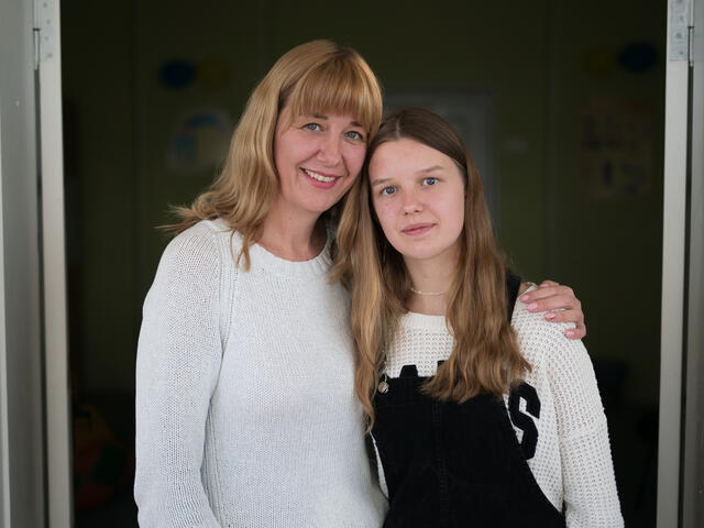 Mother and daughter stand facing the camera.