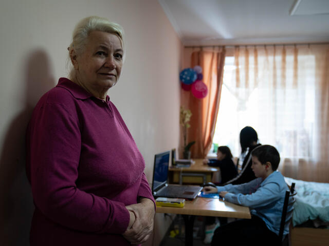 Valentina stands facing the camera, with her daughter and grandson in the background.