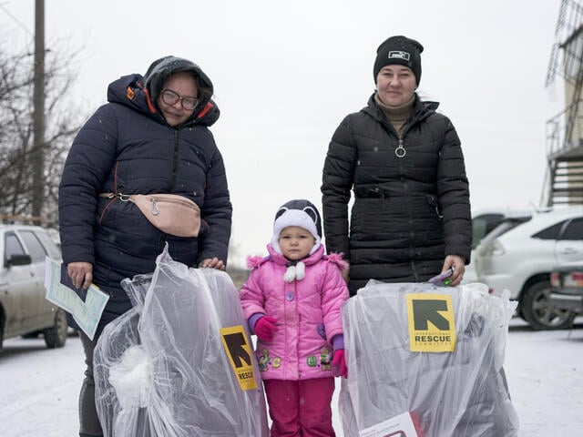 Two women stand with young girl between them, after both receiving winter kits from the IRC.