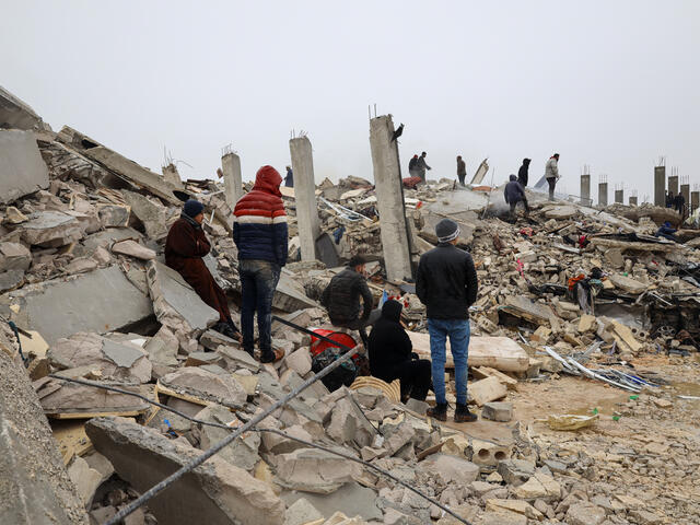 A group of survivors standing in rubble following the February 2023 earthquake in Syria.