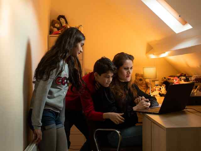 A woman sitting at a desk in front of a laptop, and two children standing next to her