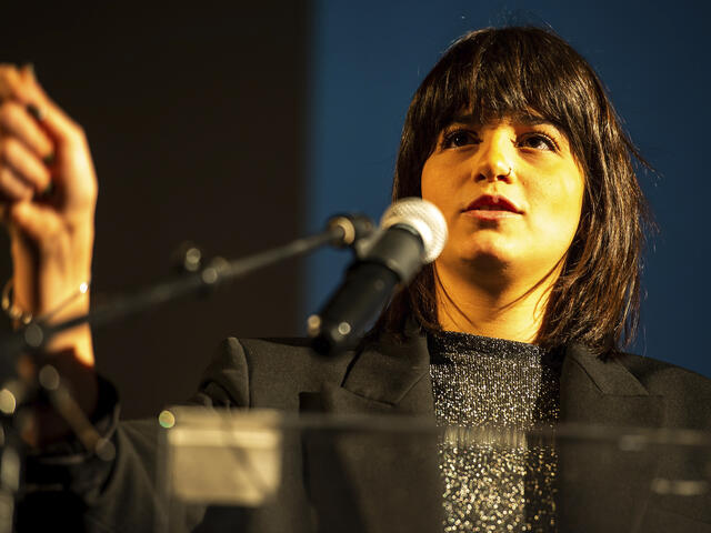 Sara speaking into a mic while giving a speech.