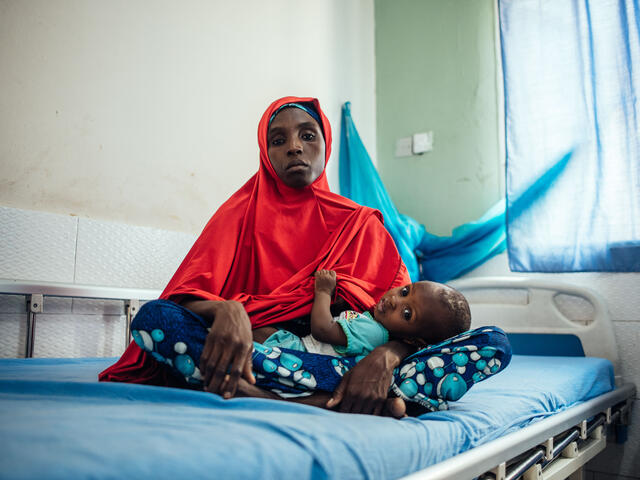 Hasfat holds her son while sitting on a bed at a medical facility in Nigeria.