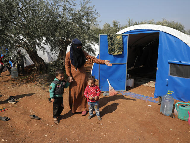 En mamma med hennes barn står framför deras tält som de fått efter jordbävningskatastrofen i Syrien.
