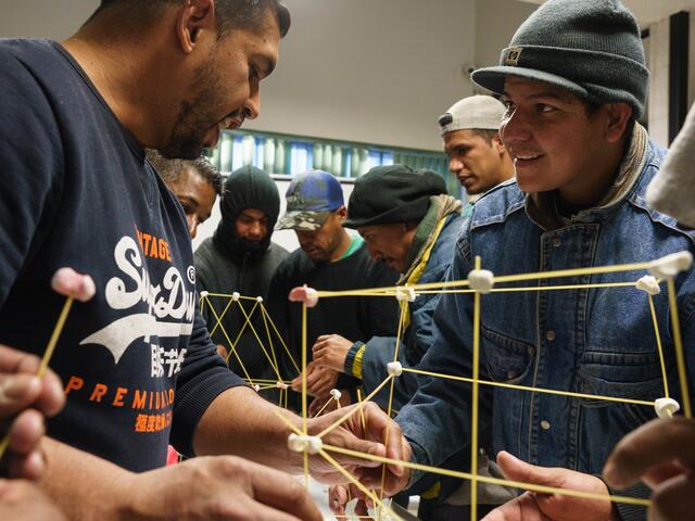 Venezuelans, Iván and Alexander, 43, participate in a group session about patience at the IRC office in Ciudad Juárez. The two men share a fun moment while carefully trying to create a tower out of spaghetti and marshmallows. 