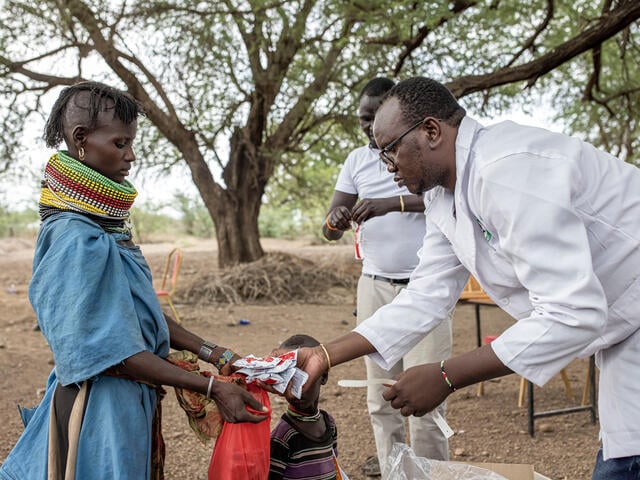 An IRC-supported health worker hands a mother several packets of PlumpyNut, a highly form of malnutrition treatment.