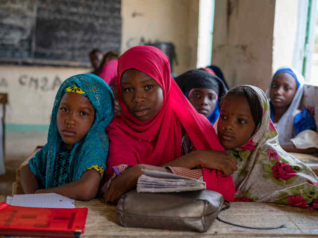 Maryama sits with two friends at a desk in class.