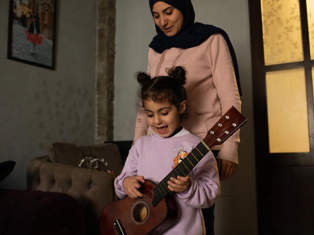Ala'a stands behind her 5-year-old daughter, Imane, who plays with a guitar.