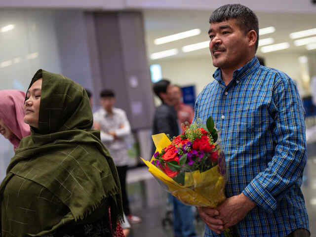 Hazar and Sanowbar wait to be reunited with their daughters; Hazar holds a bouquet of flowers.