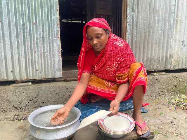 En kvinna i Bangladesh tvättar sina händer i vatten som står i en skål på marken.