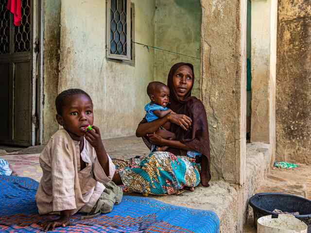 Fatima holds her 9 month-old son close in her arms. Next to them sits a young boy, Fatima's other son.