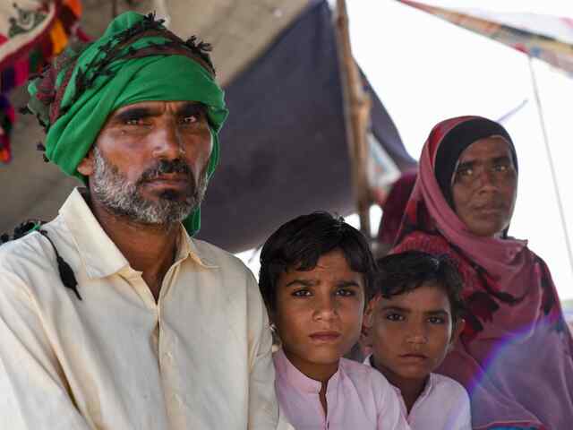 Farzana, Ghulam and their two children sit underneath a temporary shelter after the 2022 flood in Pakistan.