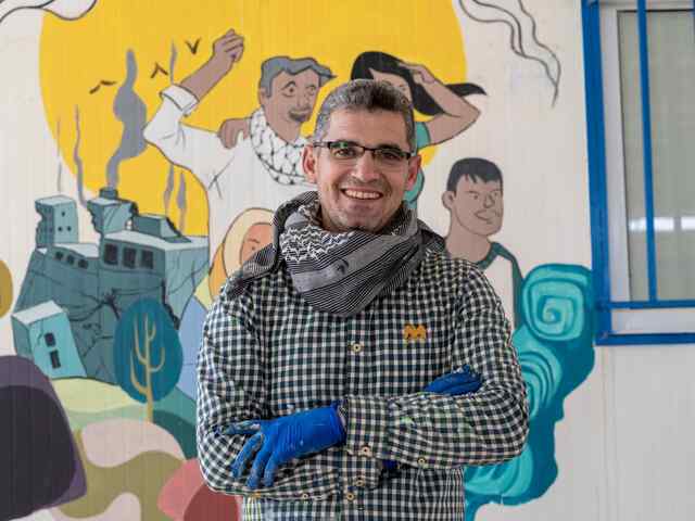 A portrait of an artist, Muhammad who poses in front of a colorful mural he created.