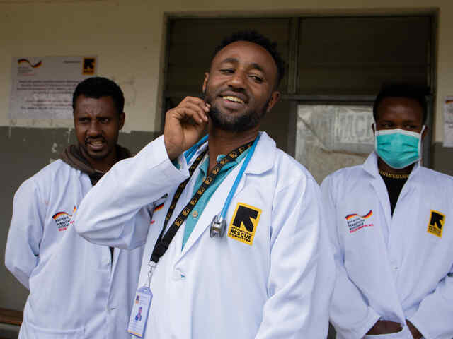 Ein Arzt telefoniert, eine Gruppe anderer Ärzte ist hinter ihm zu sehen.