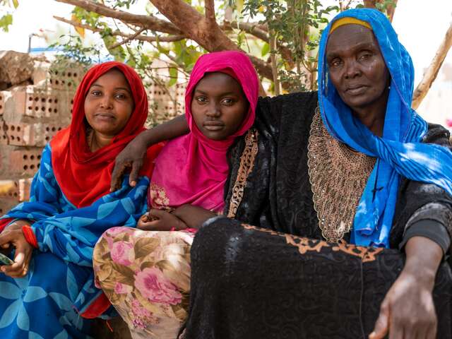 A mother and two daughters stare solemnly into the camera while posing for a portrait.