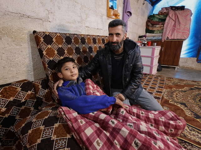 En son, Yahya*, 15, sitter med hans pappa Khaled* i deras tält.