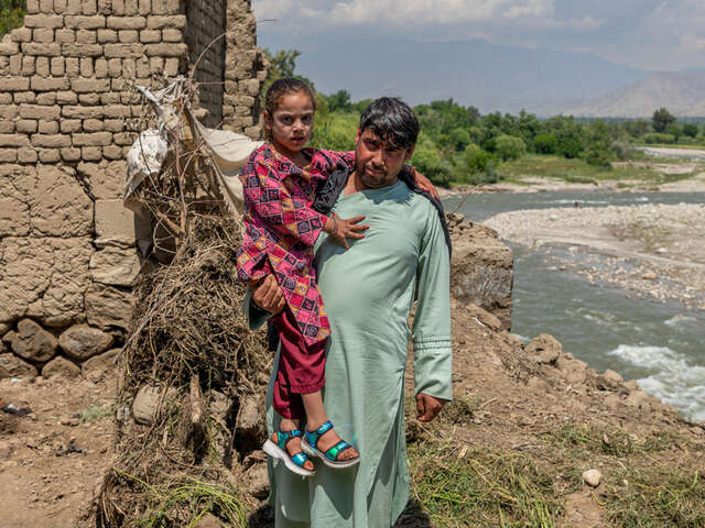 Pappa och dotter i Afghanistan står vid familjens hem som förstörts översvämningar. 