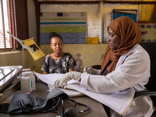 En barnmorska på RESCUE:s klinik i Sudan sitter vid ett bord bredvid en kvinnlig patient.