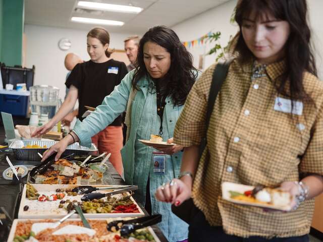 Three guests in the photo make their way through a small-bite buffet, picking out food from large trays donated by local businesses. 