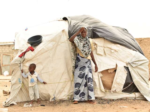 En mamma och hennes son står utanför sitt provisoriska skydd i Burkina Faso.