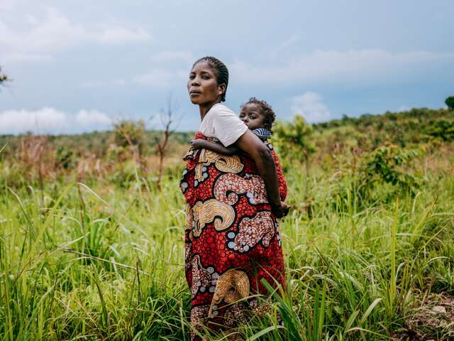 En mamma håller sitt lilla barn och går genom ett fält i Demokratiska republiken Kongo.