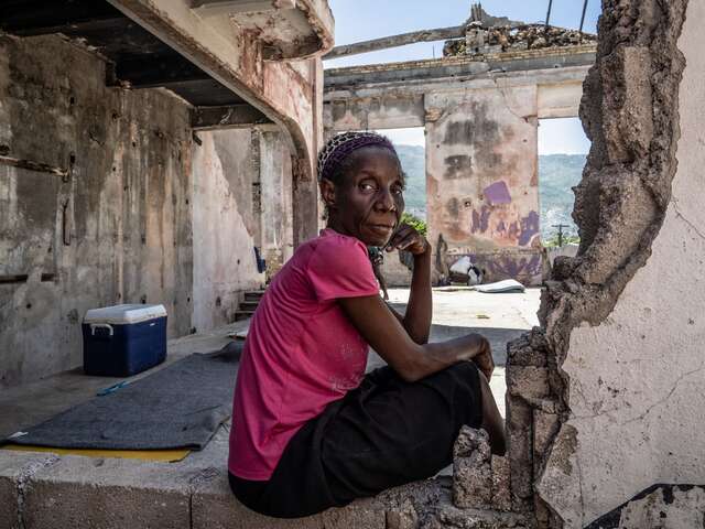 En kvinna poserar för ett foto bland ruinerna av en byggnad i Haiti.