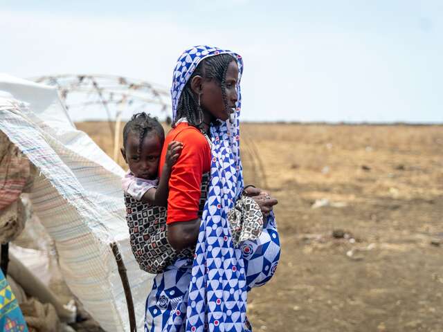 En mamma bär sitt barn medan hon lämnar deras provisoriska skydd i Sudan.