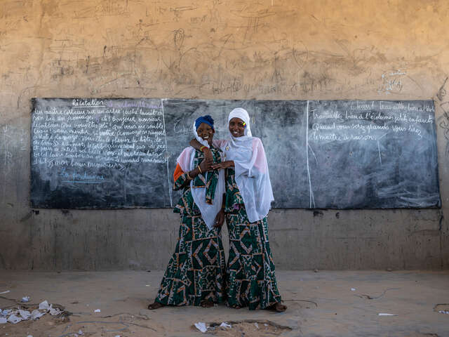 Två tjejer står framför en griffeltavla och ler. 