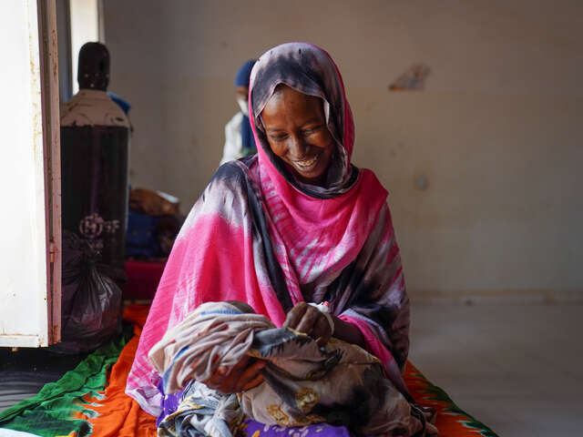 En mamma håller i sin bebis och ler. 