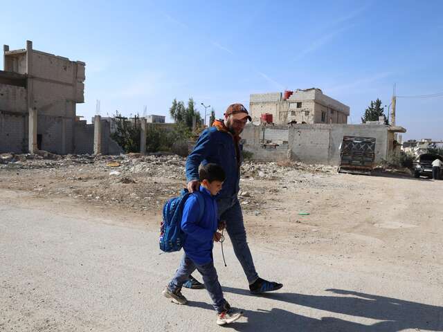 Al-Qusayr, Homs province, Syria. Mohammad, 38, walks with his older son Adam toward school. For Syrian families like theirs, education is a vital pathway to hope, stability, and a brighter future despite the challenges of return.
