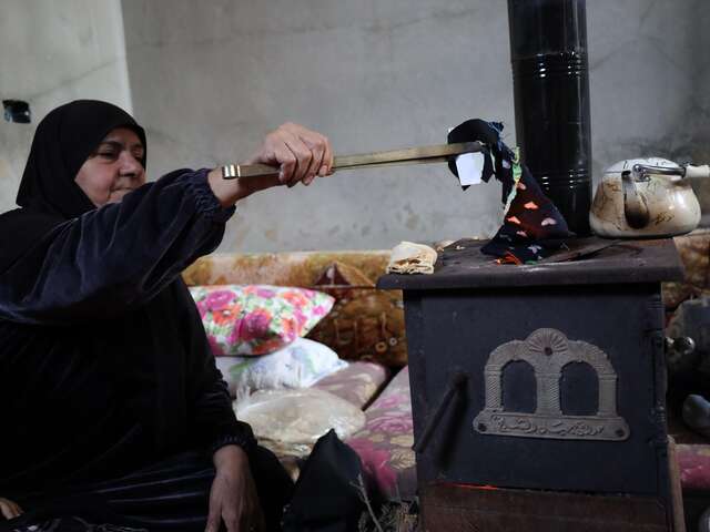 Al-Qusayr, Homs province, Syria. Bayan's mother puts old textiles into the stove for heat. Since fuel remains scarce and costly, families like Bayan’s  often have to burn whatever they can find to stay warm.