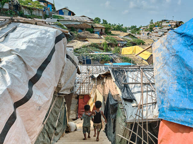 Två små pojkar håller om varandra och går genom ett trångt flyktingläger.