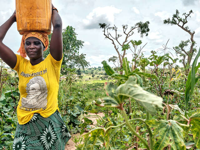 Daguidam går genom ett fält och bär en hink på huvudet.