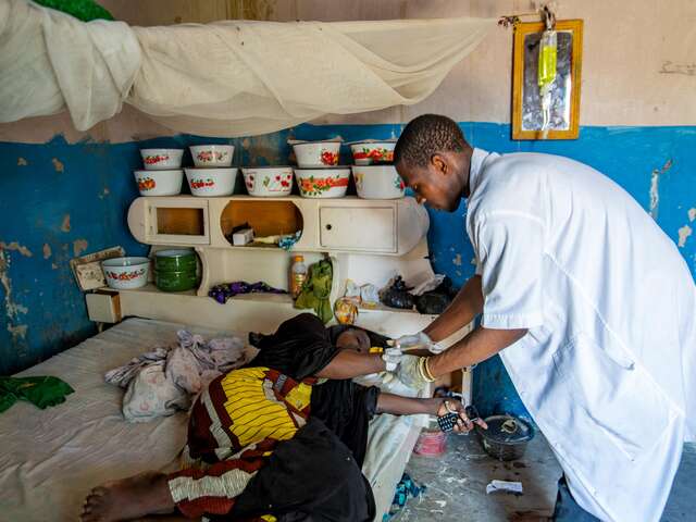 Doctor providing care to a woman laying down on her bed 