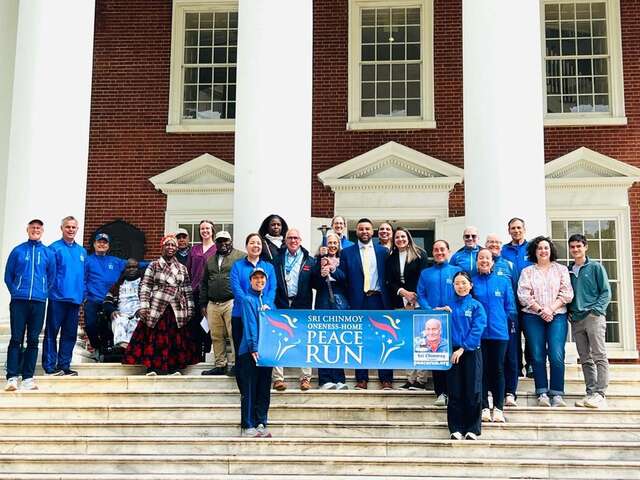 large group standing on steps of Rotunda holding blue banner