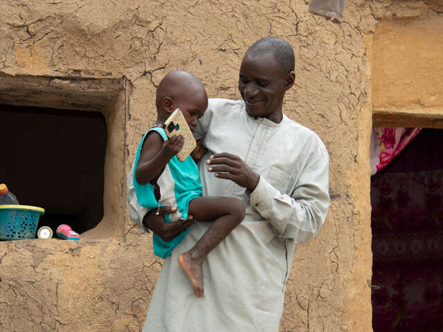 Hamar Ag Halada Traoré, 50, steht lächelnd mit seinem Kind da, Tenenkou, Mali.
