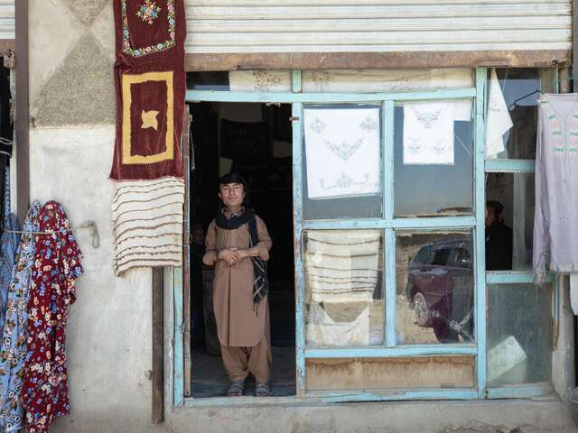 Darweza stands at the entrance of the tailor shop where he works. 