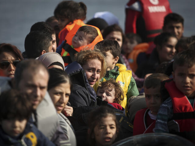 Syrian refugees, including women and children,  approach the shores of Lesbos, Greece in an overcrowded rubber raft.