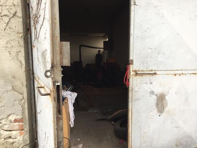 A young refugee boy inside an abandoned warehouse that is dark and unheated but serves as a refugee shelter.