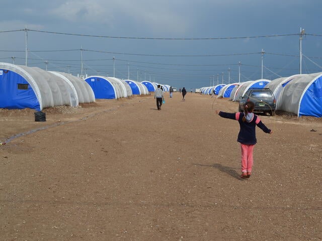 Children play among rows of tents set on sandy soil in Nargilzila camp.