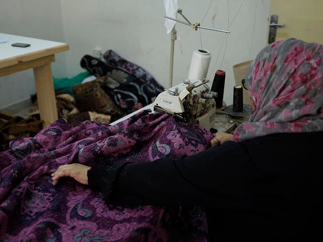 A woman works at a sewing machine at her family's newly restarted upholstery business in Jordan 